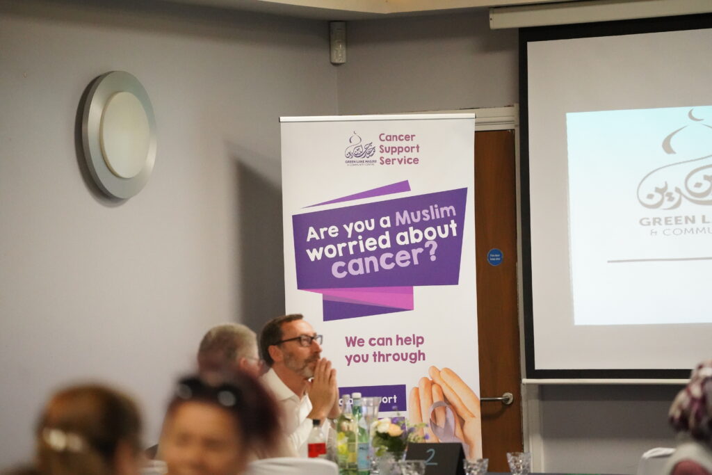 Photo from a symposium for the project hosted at GLM. Featuring project PI Peter Morey in front of a poster titled "GLM Cancer support service. Are you a Muslim worried about cancer? We can help you through."