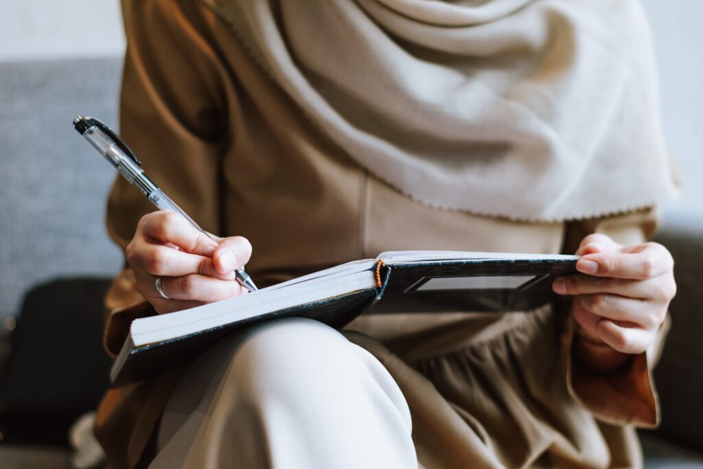 a young woman seated with a notebook and pen writing something down.